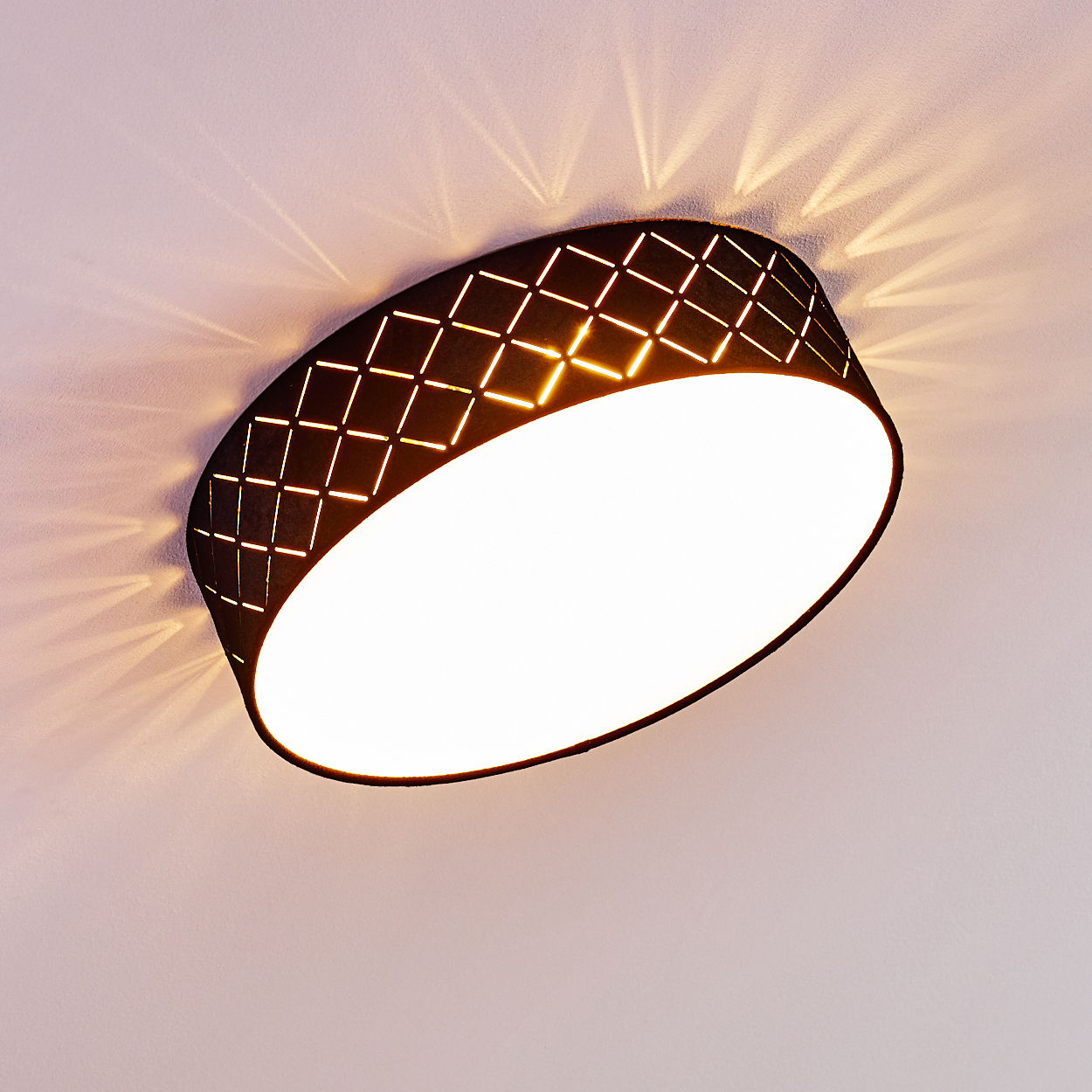 Eine schwarze Deckenlampe mit Rautenmuster, die helles Licht aussendet. Licht scheint auf die weiße Decke. Die Lampe ist rund.