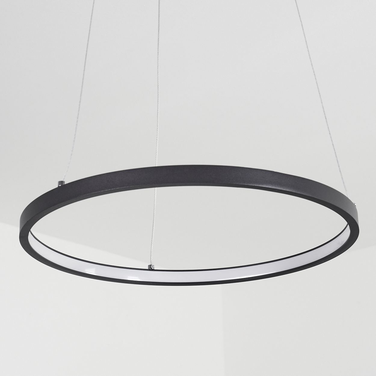 Eine schwarze, kreisförmige Leuchte hängt an dünnen Kabeln von der Decke. Sie hat ein weißes Innenlicht.