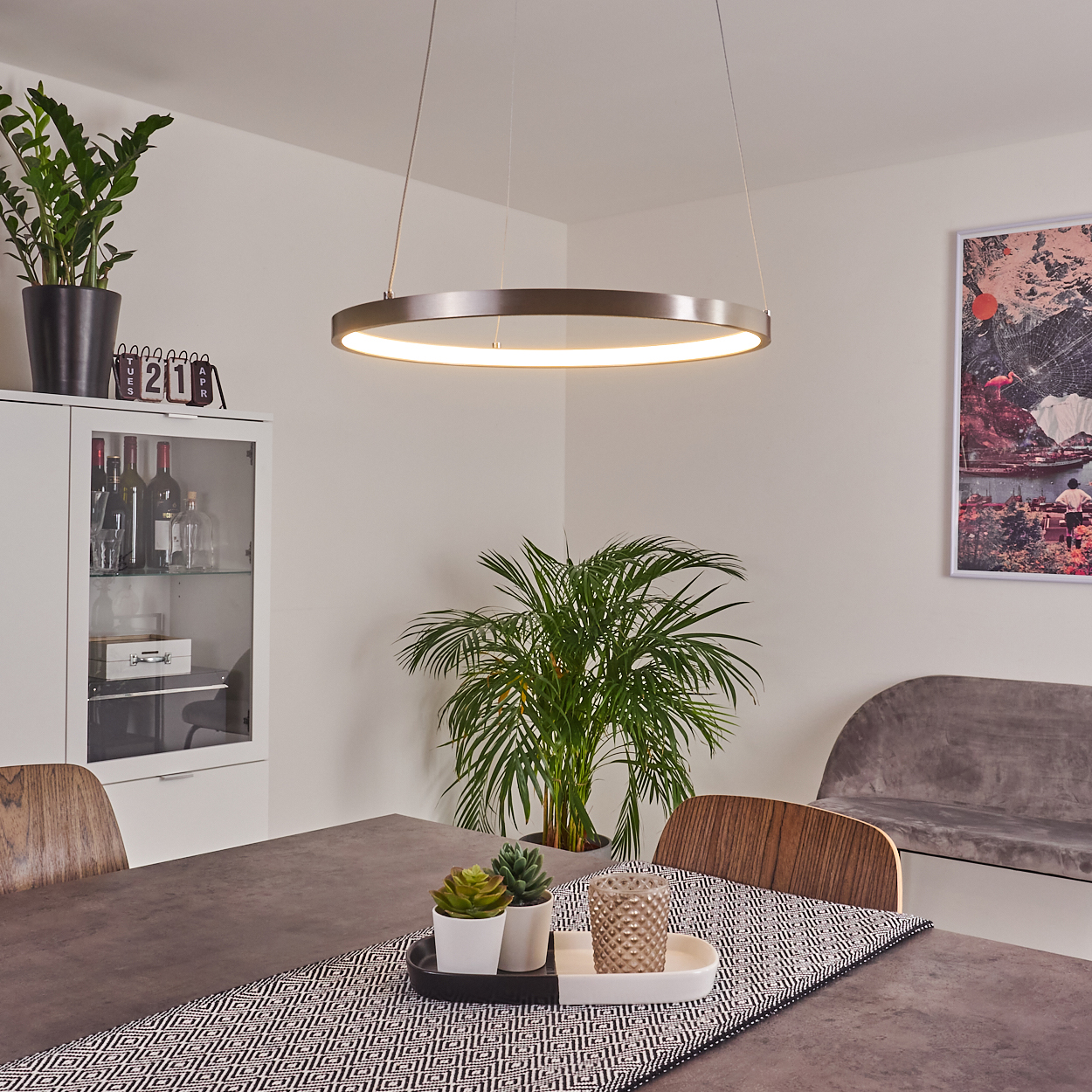 Ein Esszimmer mit Tisch, Pflanzen und kreisförmiger Leuchte. Ein Gemälde hängt an der Wand.
