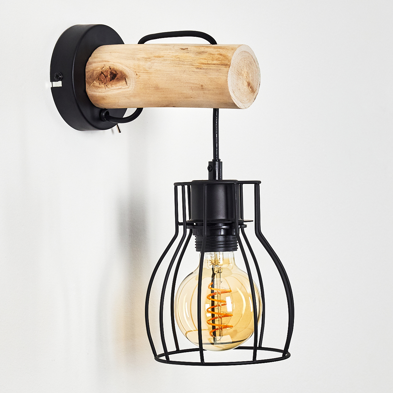 Eine Wandlampe. Sie hat einen Holzbalken, einen schwarzen Metallkäfig und eine Glühbirne. Der Hintergrund ist eine weiße Wand.