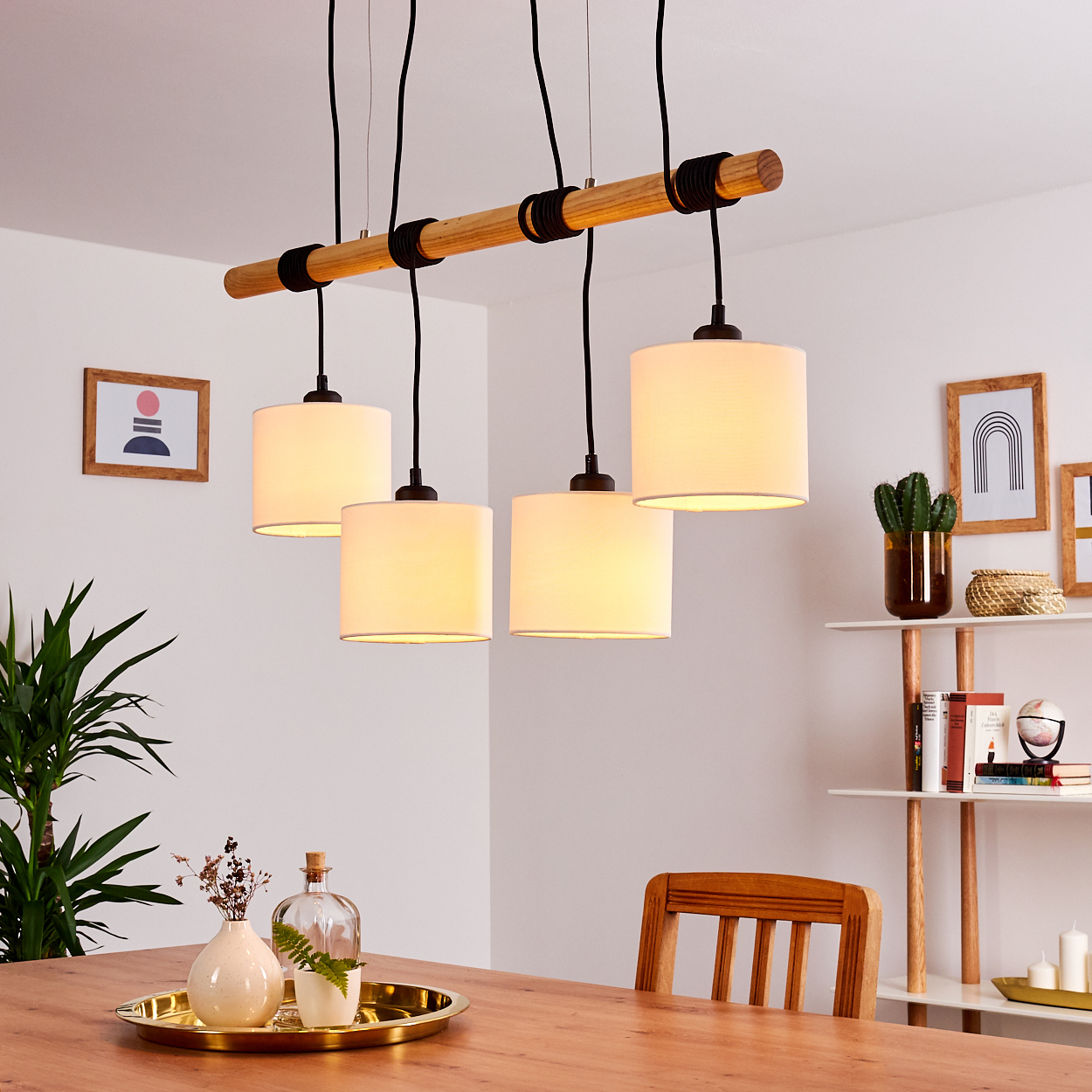 Ein Esszimmer mit Holztisch, vier Pendelleuchten, einer Pflanze und Dekoartikeln auf einem Regal.