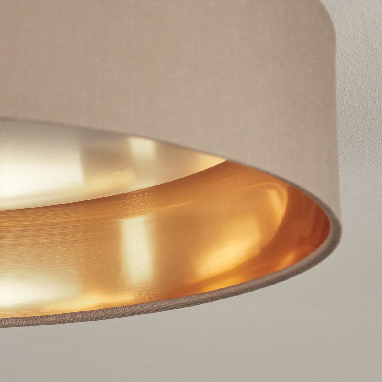 Nahaufnahme einer Lampe. Beiger Lampenschirm mit goldener Innenseite. Der Hintergrund ist eine weiße Decke.