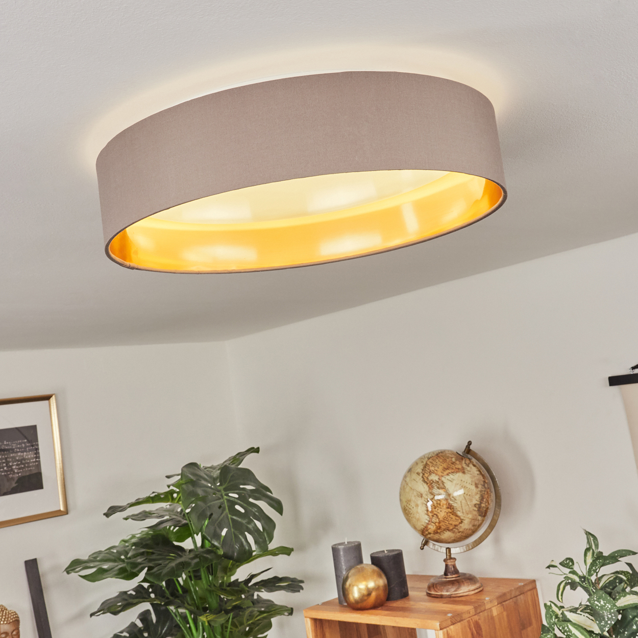 Eine Deckenlampe mit beigem Schirm ist beleuchtet. Darunter ein Tisch mit Globus, Kerzen und Pflanzen.