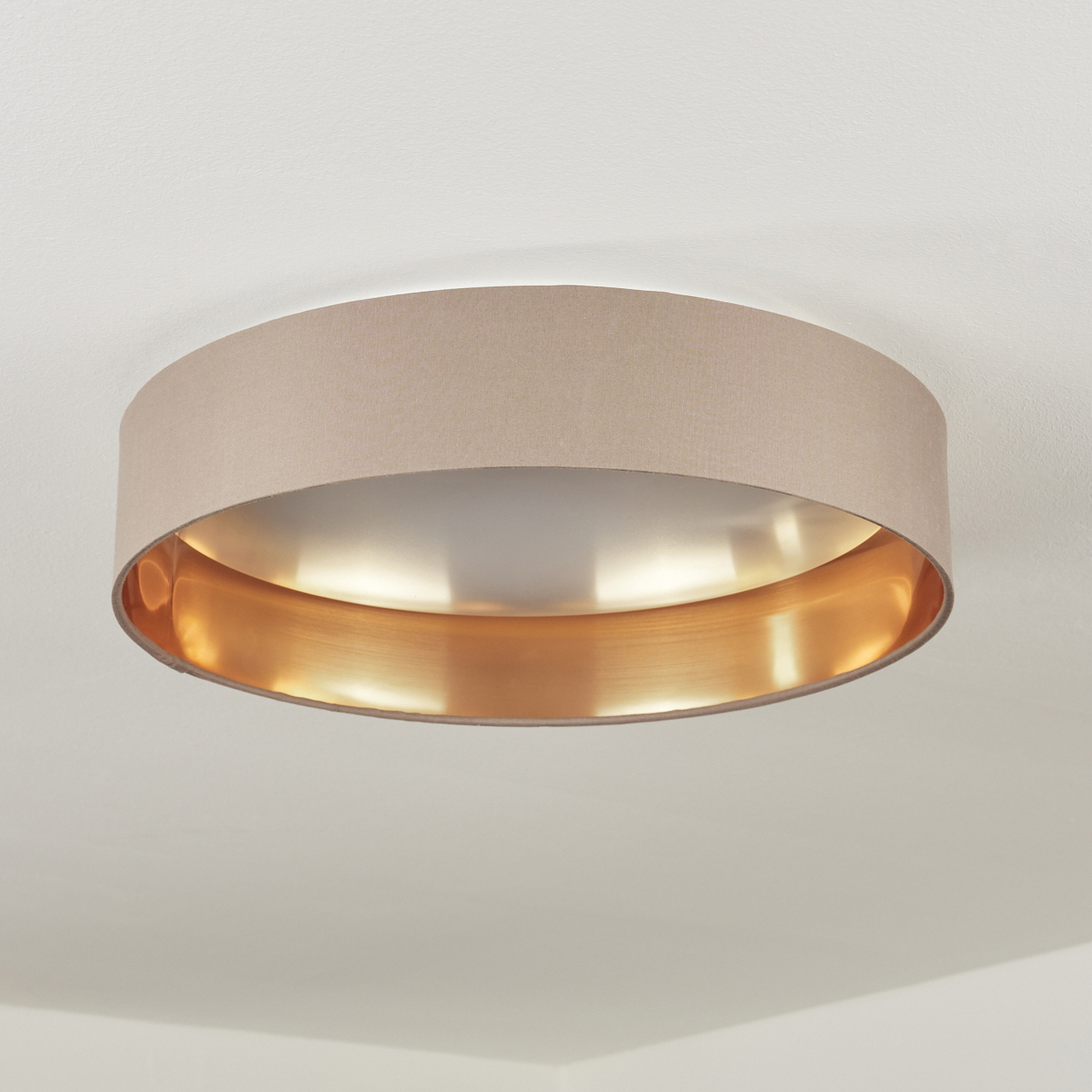 Eine runde Deckenlampe mit beigem Schirm und goldenem Innenraum. Die Lampe ist an einer weißen Decke befestigt.