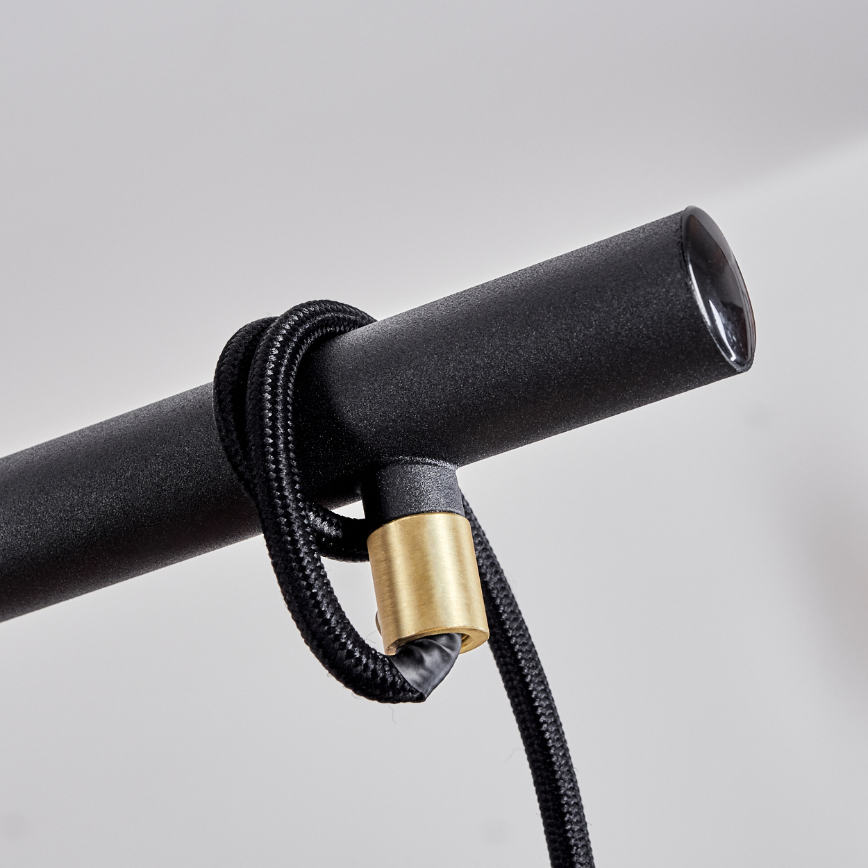 Nahaufnahme einer schwarzen Metalllampe. Ein geflochtenes schwarzes Kabel wickelt sich um das Metall und ist mit einem goldfarbenen Zylinder verbunden.