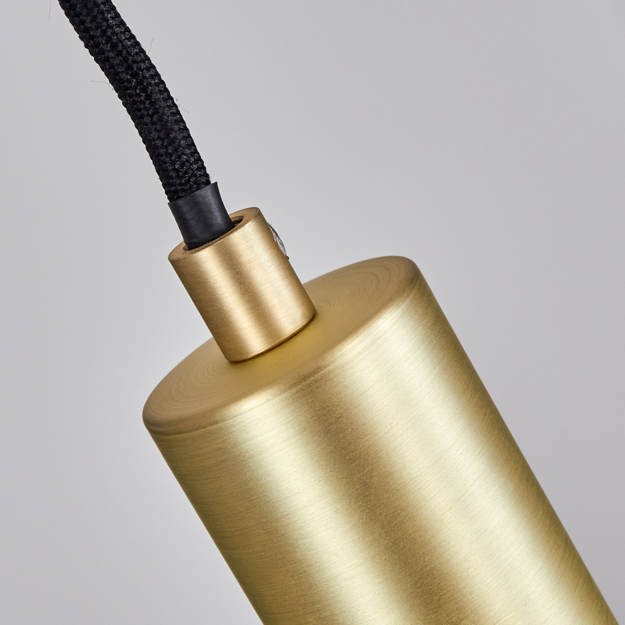 Nahaufnahme eines Messingzylinders und -anschlusses mit einem schwarzen geflochtenen Kabel vor grauem Hintergrund.