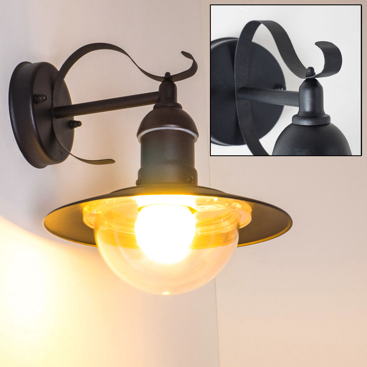 Schwarze Wandlampe mit gelblich getönter Glaskugel und Metallschirm. Die Lampe befindet sich vor einer weißen Wand.