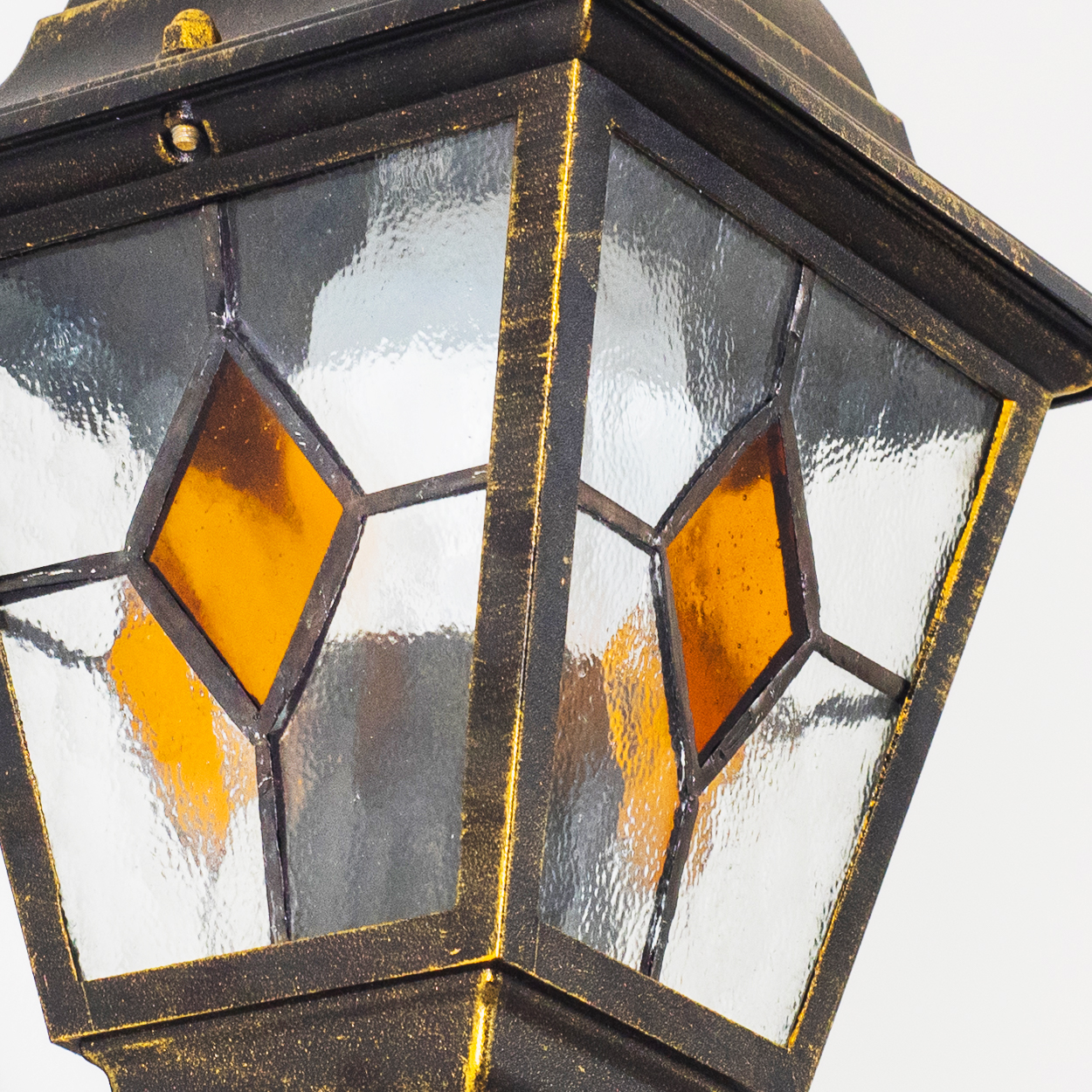 Nahaufnahme einer dekorativen Außenlampe. Sie hat einen schwarzen Metallrahmen mit goldenen Akzenten und Glasscheiben. Zwei bernsteinfarbene Diamanten sind sichtbar.