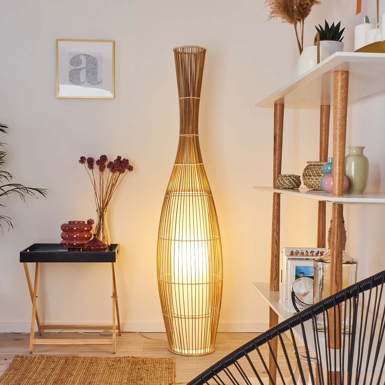Eine gewebte Stehlampe ist der Mittelpunkt. Ein Tabletttisch mit Dekoration steht in der Nähe eines Teppichs. Ein Regal mit Vasen und Dekoration ist sichtbar.