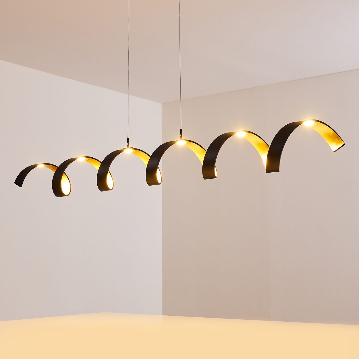 Eine moderne Hängelampe mit einer Reihe von schwarzen, bogenförmigen Lichtern mit goldenen Innenräumen. Die Lichter hängen von der Decke.