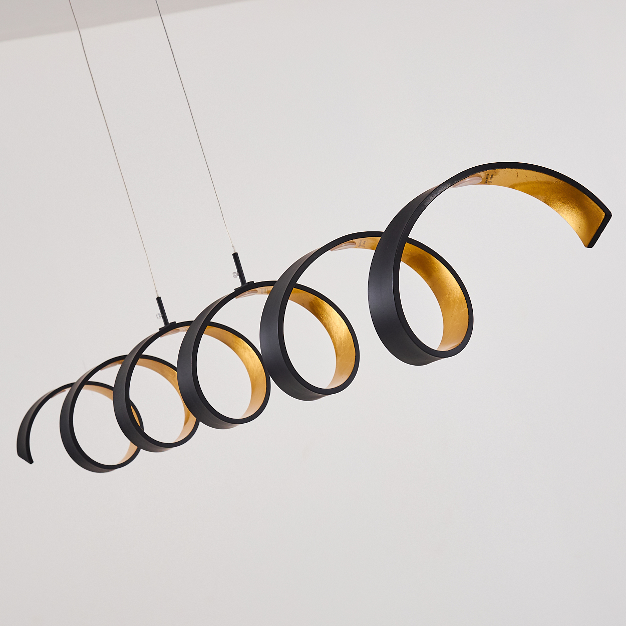 Eine moderne, schwarz-goldene Spirallampe hängt vor einem weißen Hintergrund. Das Licht wird von dünnen Drähten getragen.