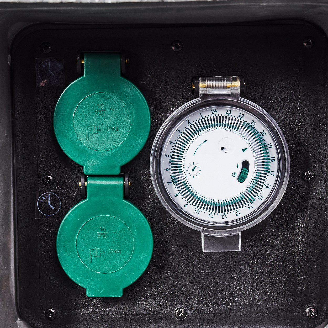 Nahaufnahme einer schwarzen Elektrokiste mit zwei grünen Abdeckungen und einem Timer-Zifferblatt. Das Zifferblatt hat Zahlen und einen kleinen Pfeil.