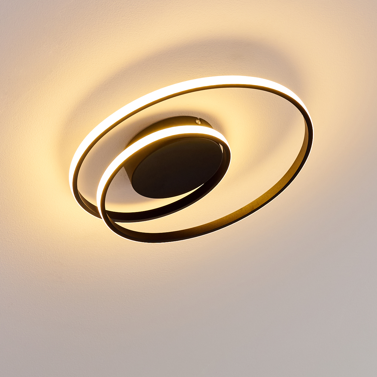 Eine moderne Deckenleuchte mit schwarzem Sockel und spiralförmigem, beleuchtetem Rahmen, der ein warmes Licht wirft.
