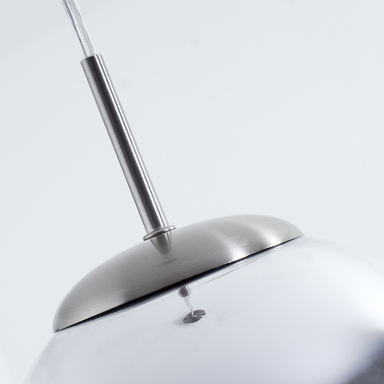 Nahaufnahme einer metallischen Pendelleuchte. Die Lampe hat einen silbernen, kuppelförmigen Schirm, eine silberne Stange und ein transparentes Kabel auf weißem Hintergrund.