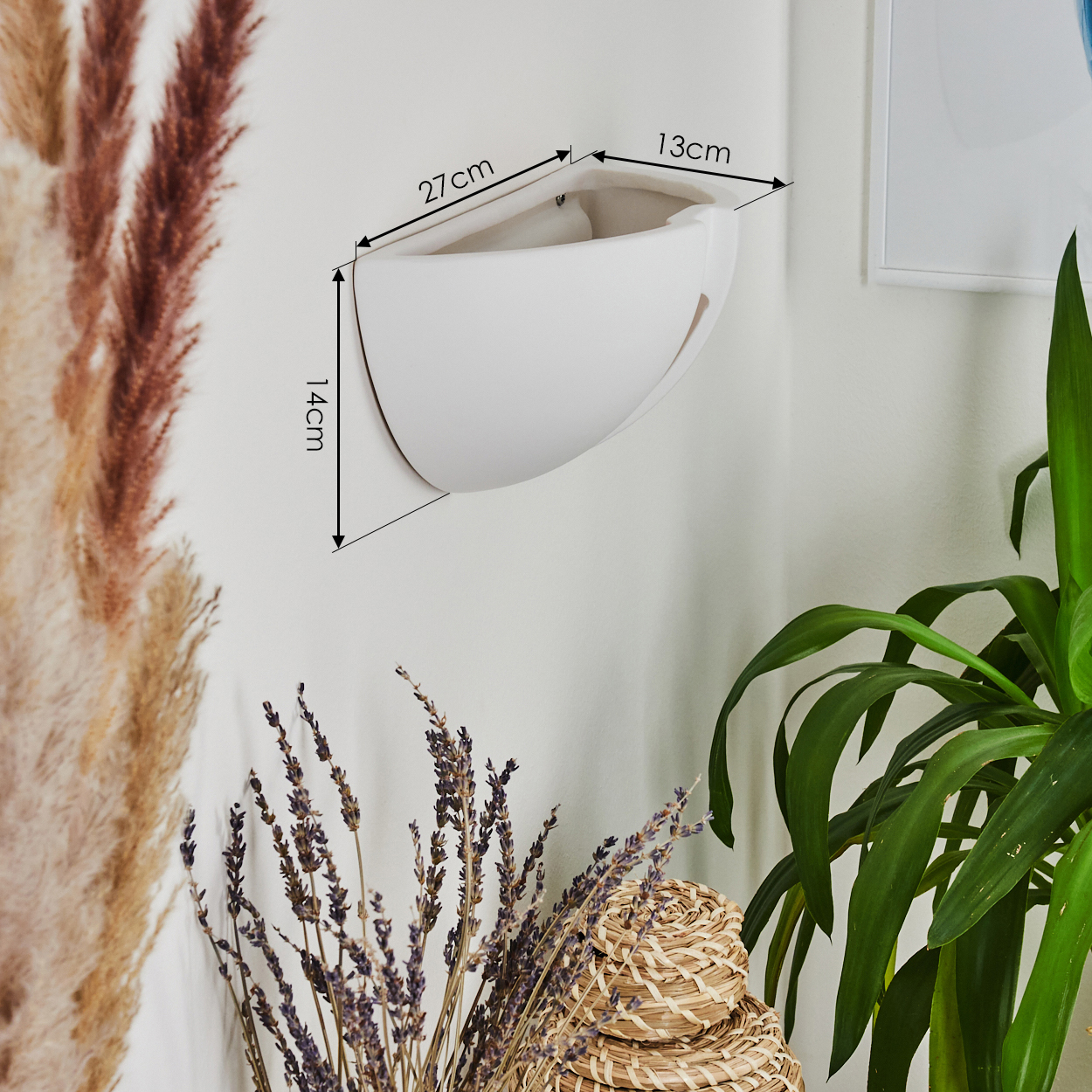 Ein weißer Wandtopf mit Maßen, umgeben von Pflanzen, Lavendel und einem Weidenkorb. Der Hintergrund ist eine weiße Wand.