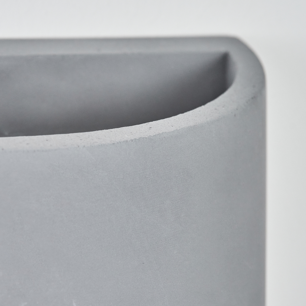 Nahaufnahme eines grauen Beton-Stiftehalters. Der Halter hat eine abgerundete Oberseite und ein quadratisches Inneres. Der Hintergrund ist weiß.