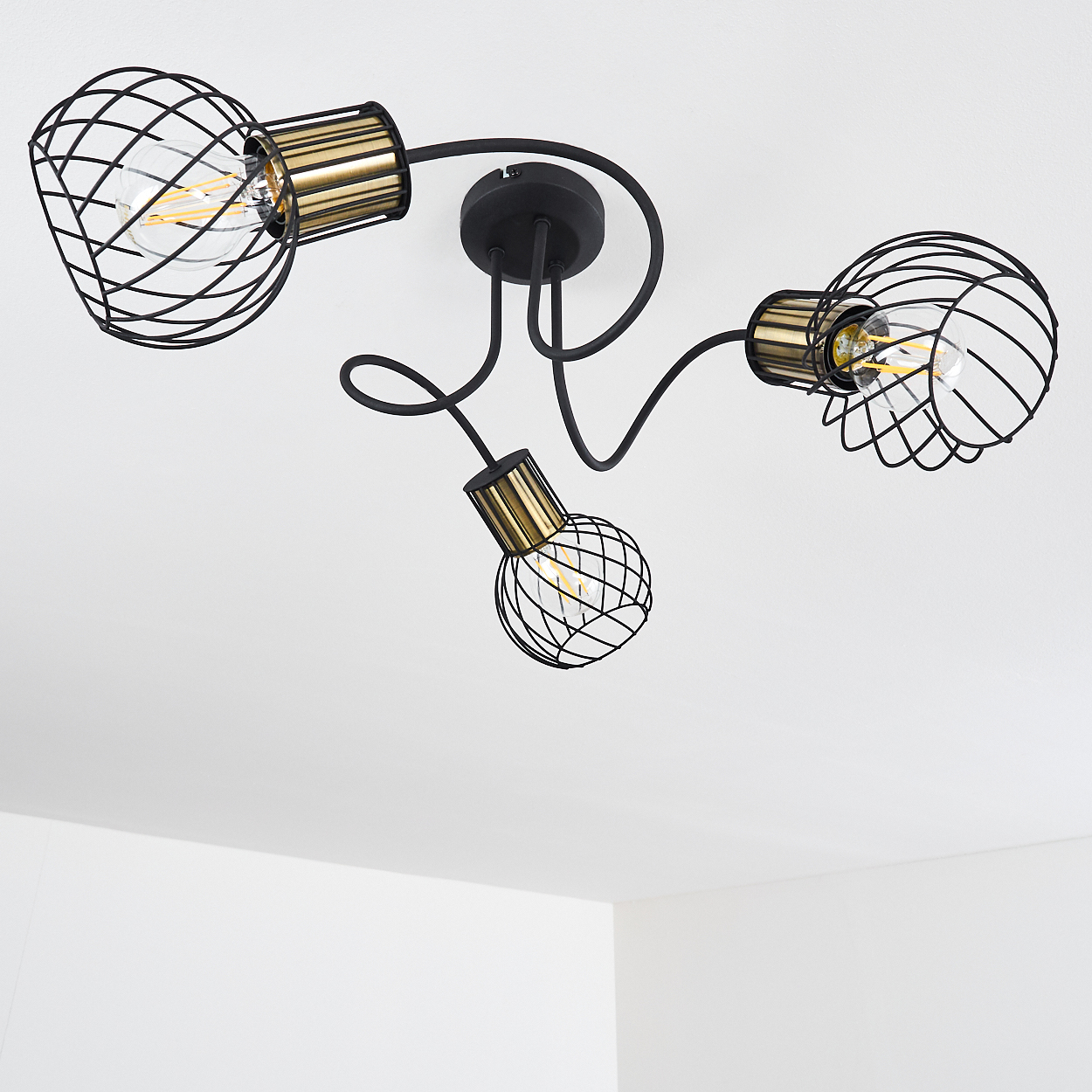 Eine schwarze Deckenlampe mit drei Lichtern. Jedes Licht hat einen Drahtkäfigschirm und goldene Akzente. Der Hintergrund ist eine weiße Decke.