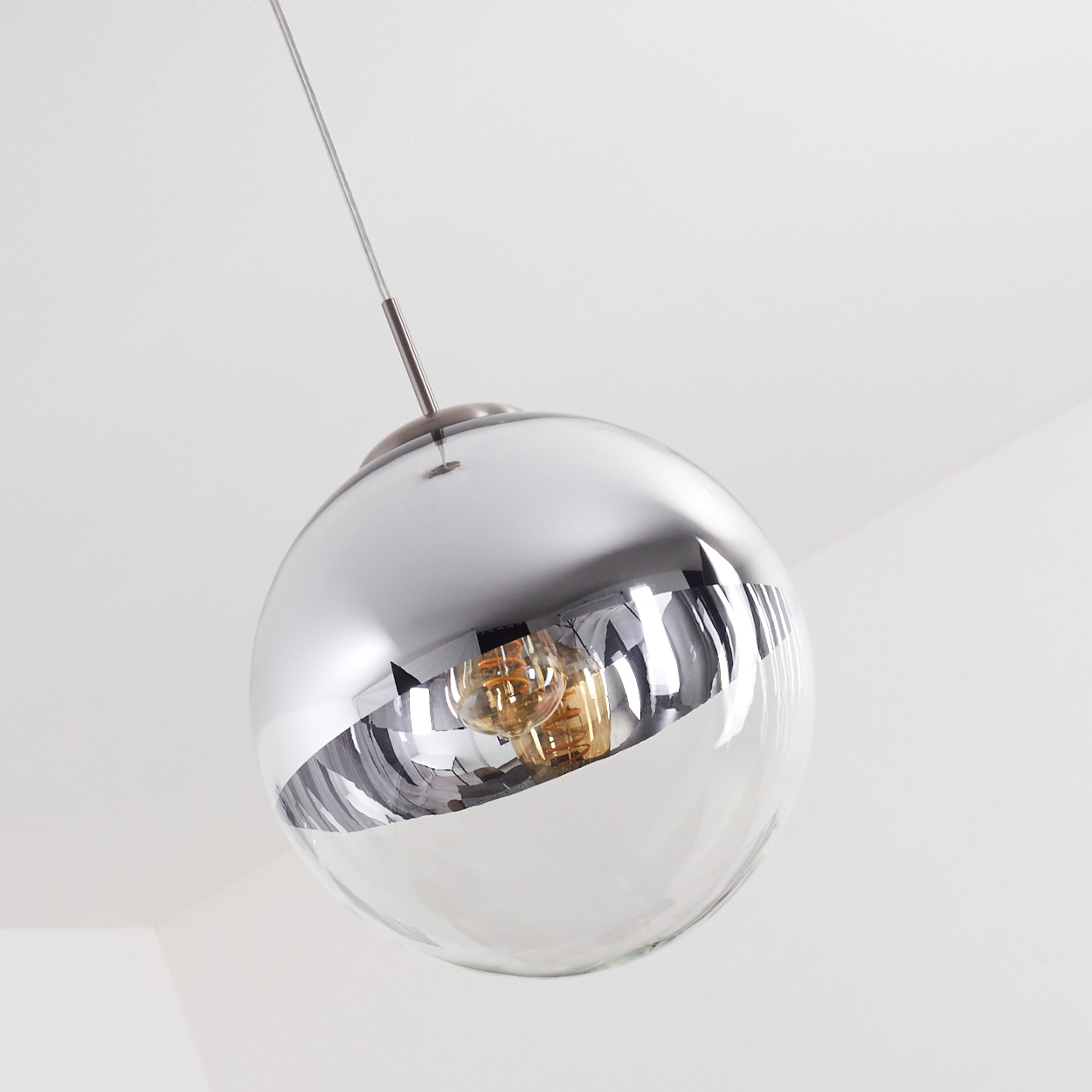 Eine moderne, kugelförmige Pendelleuchte mit silberner, reflektierender Oberseite und klarer Unterseite. Die Glühbirne ist innen sichtbar.
