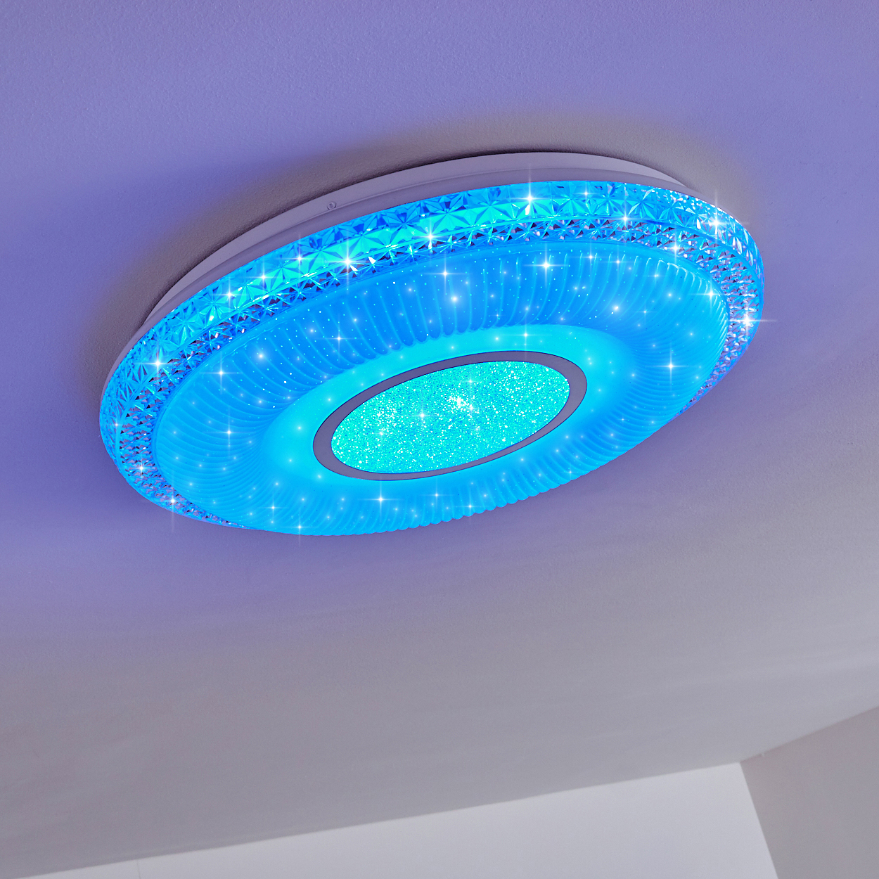 Blaue LED-Deckenleuchte. Ovale Form mit funkelndem Zentrum. Das Licht ist von einem gemusterten Rand umgeben, montiert an einer weißen Decke.