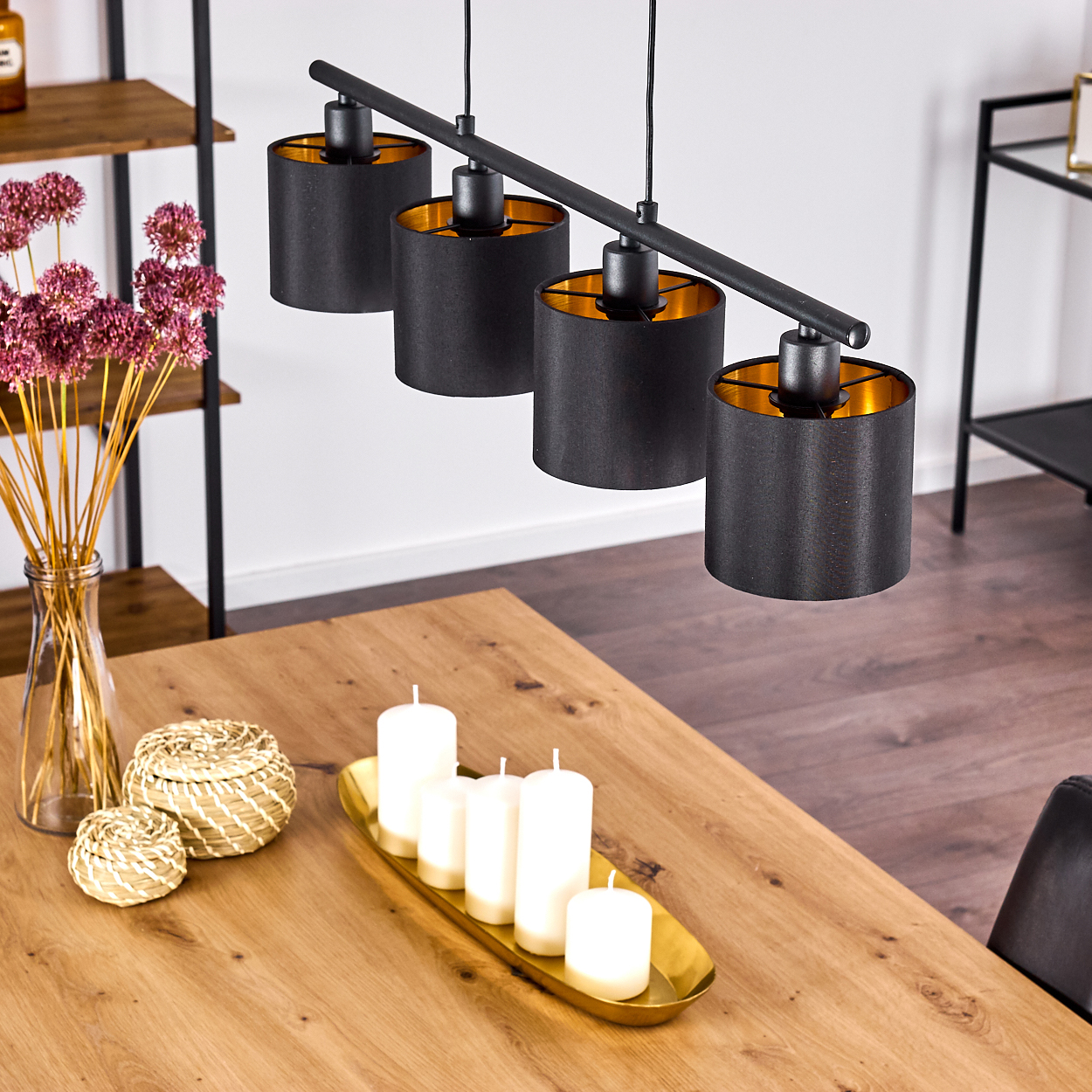 Esszimmer mit Holztisch, schwarzen Lampen und Kerzen. Trockenblumen in einer Vase und dekorative Körbe sind ebenfalls sichtbar.