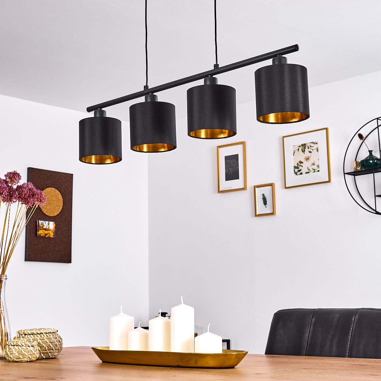 Ein modernes Esszimmer mit einem schwarzen Kronleuchter mit goldenem Innenraum, weißen Kerzen und gerahmten Bildern an der Wand.