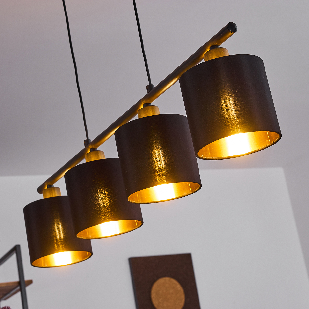 Eine moderne Deckenleuchte mit vier schwarzen Lampenschirmen. Das Innere der Schirme ist golden, der Hintergrund ist eine weiße Decke.
