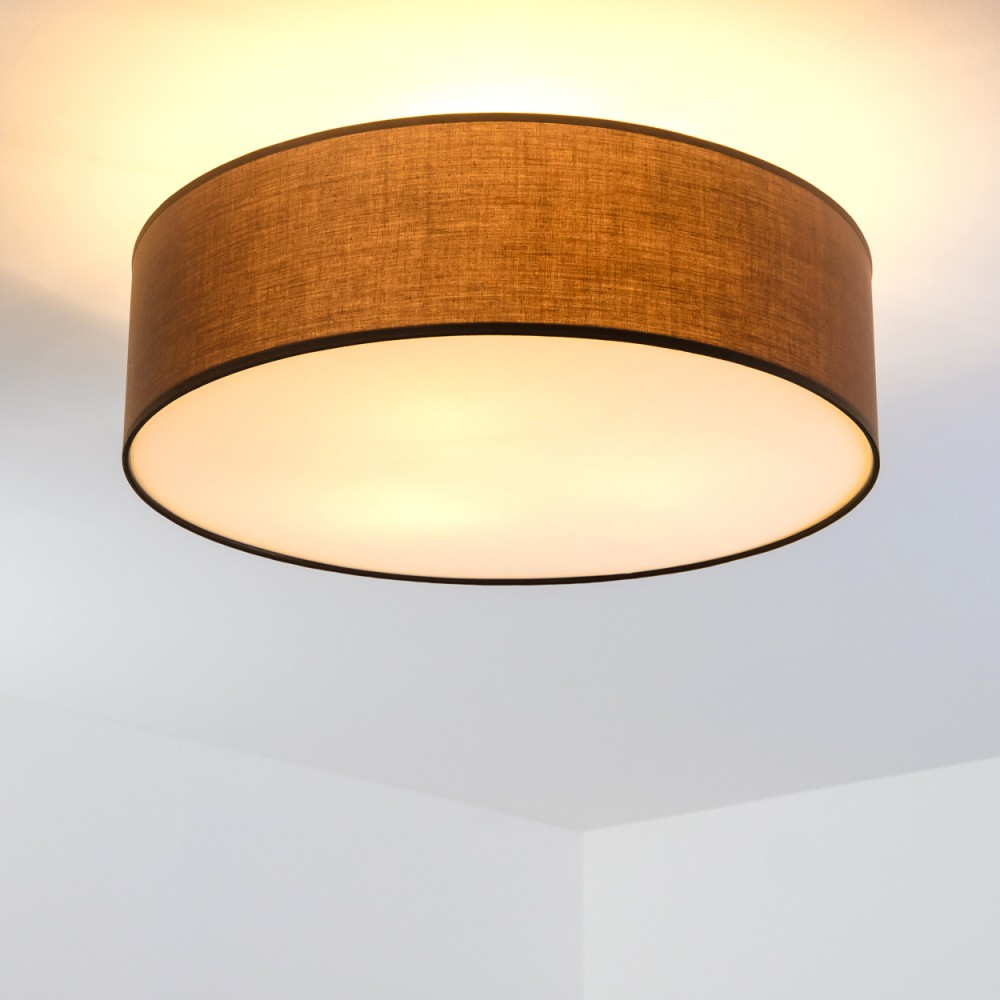 Ein brauner, zylindrischer Lampenschirm ist an einer weißen Decke befestigt. Das Licht ist an, und der Schirm hat einen schwarzen Umriss.