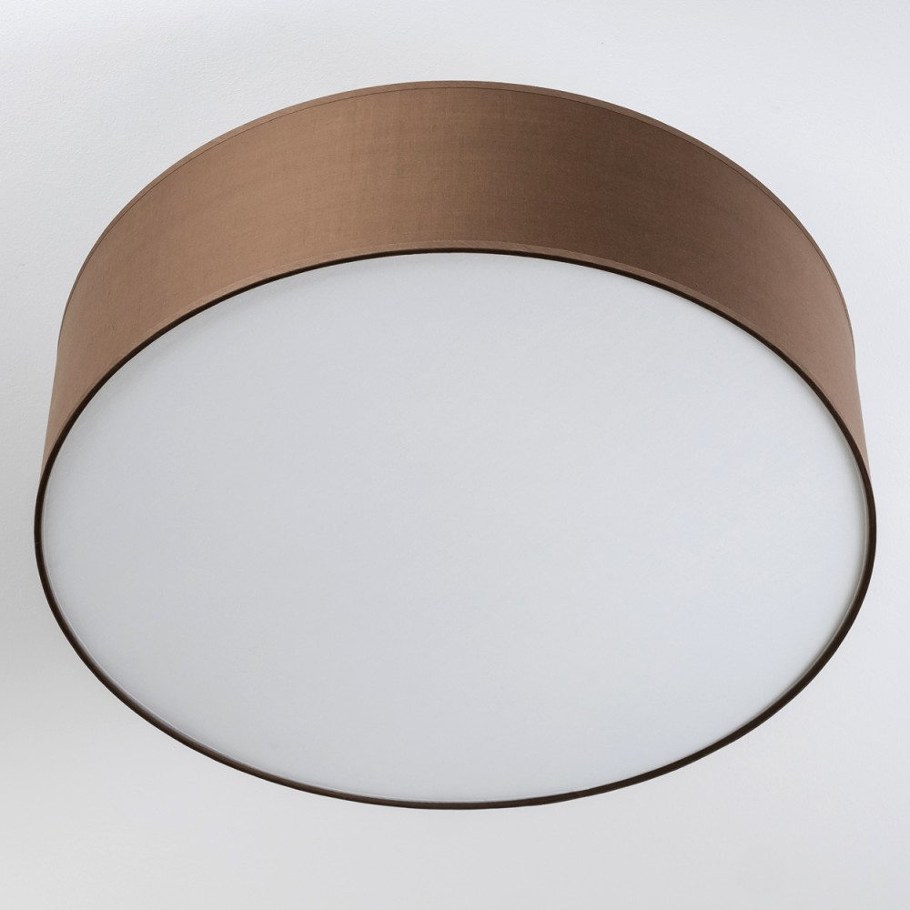Ein brauner, kreisförmiger Lampenschirm mit weißem Lichtdiffusor. Der Lampenschirm befindet sich vor einer weißen Wand.