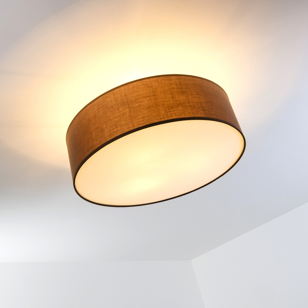Eine braune, oval geformte Deckenlampe ist an einer weißen Decke angebracht. Die Lampe strahlt ein warmes, gelbliches Licht aus.