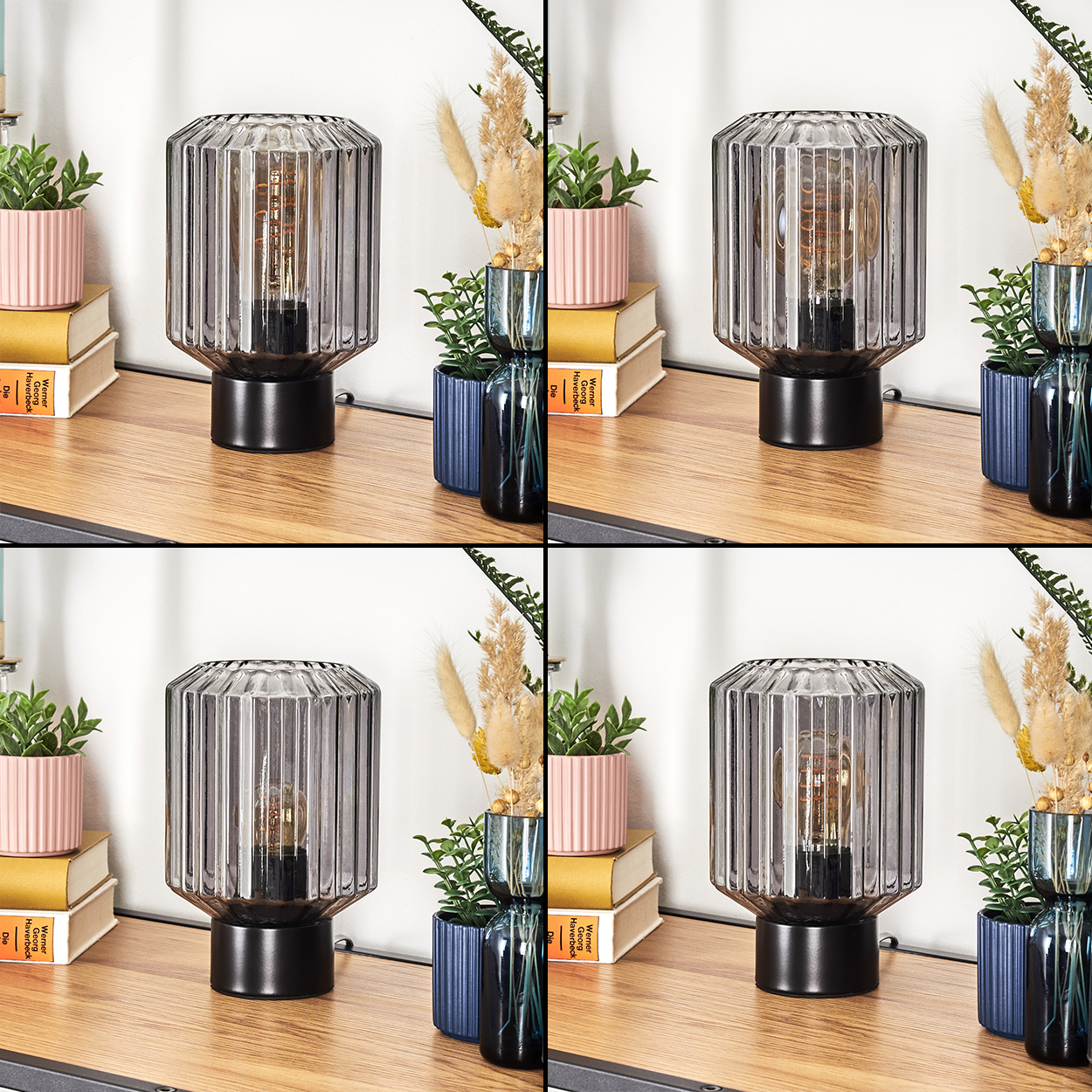 Eine graue Glaslampe auf einer Holzoberfläche, umgeben von Pflanzen und Büchern. Die Lampe hat einen schwarzen Sockel und eine sichtbare Glühbirne.