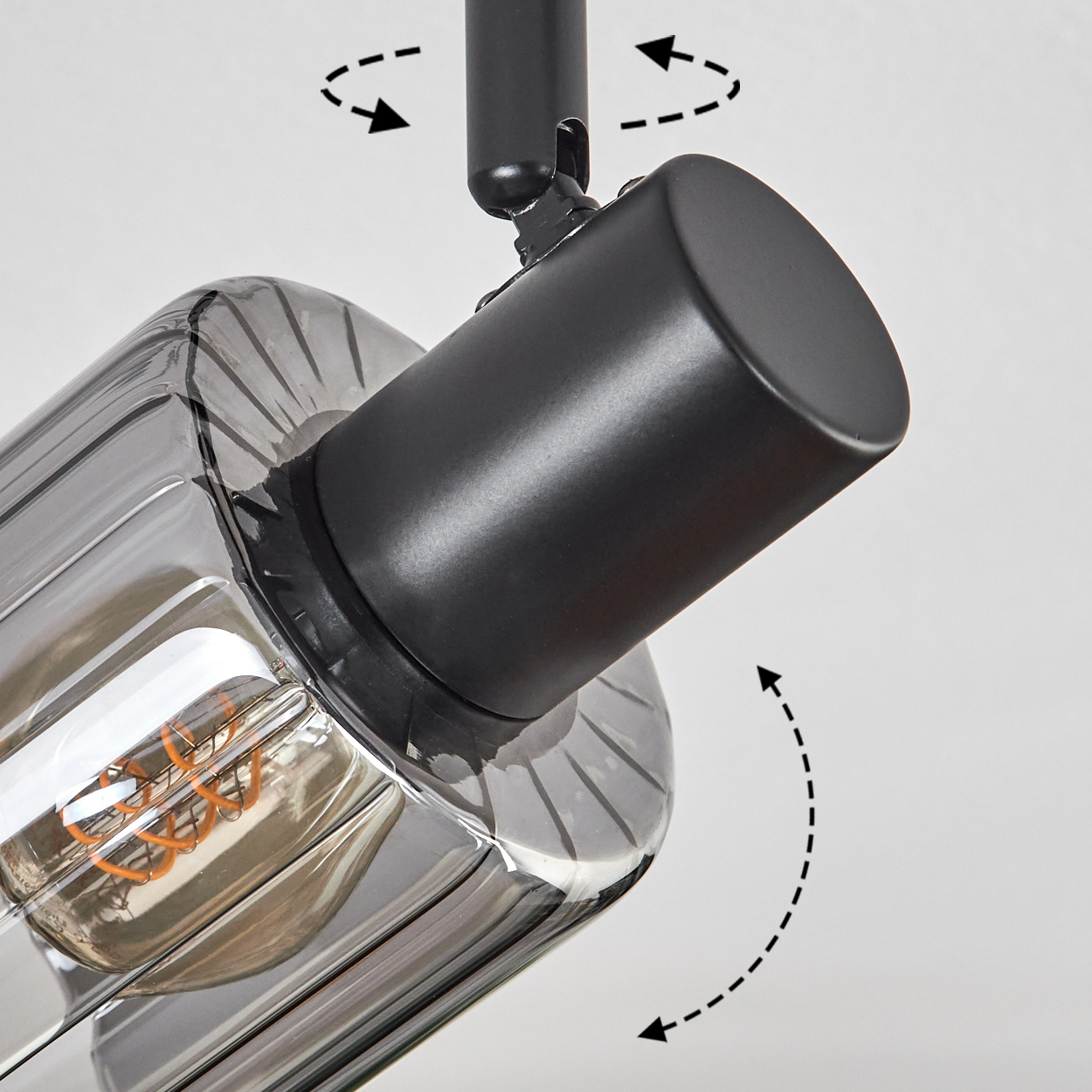 Nahaufnahme einer modernen Lampe. Sie hat einen schwarzen, zylindrischen Sockel und einen transparenten, geriffelten Glasschirm. Die Glühbirne ist sichtbar.