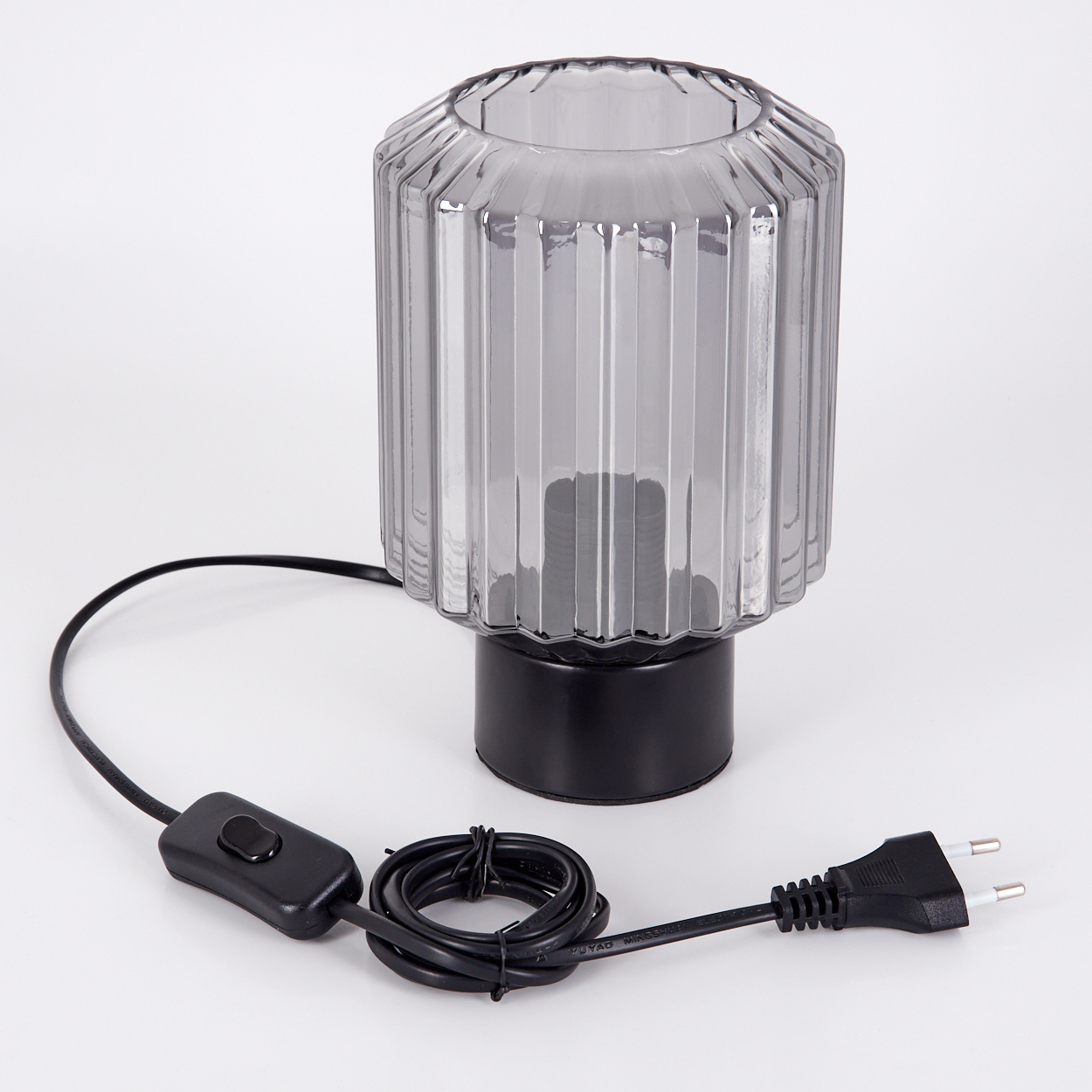 Eine graue, geriffelte Glaslampe mit schwarzem Sockel und Kabel, einem Schalter und einem Stecker auf weißem Untergrund.
