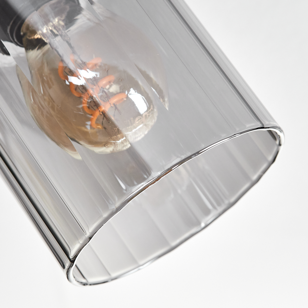 Nahaufnahme eines transparenten, grauen Glaslampenschirms mit einer Glühbirne im Inneren. Der Hintergrund ist weiß.