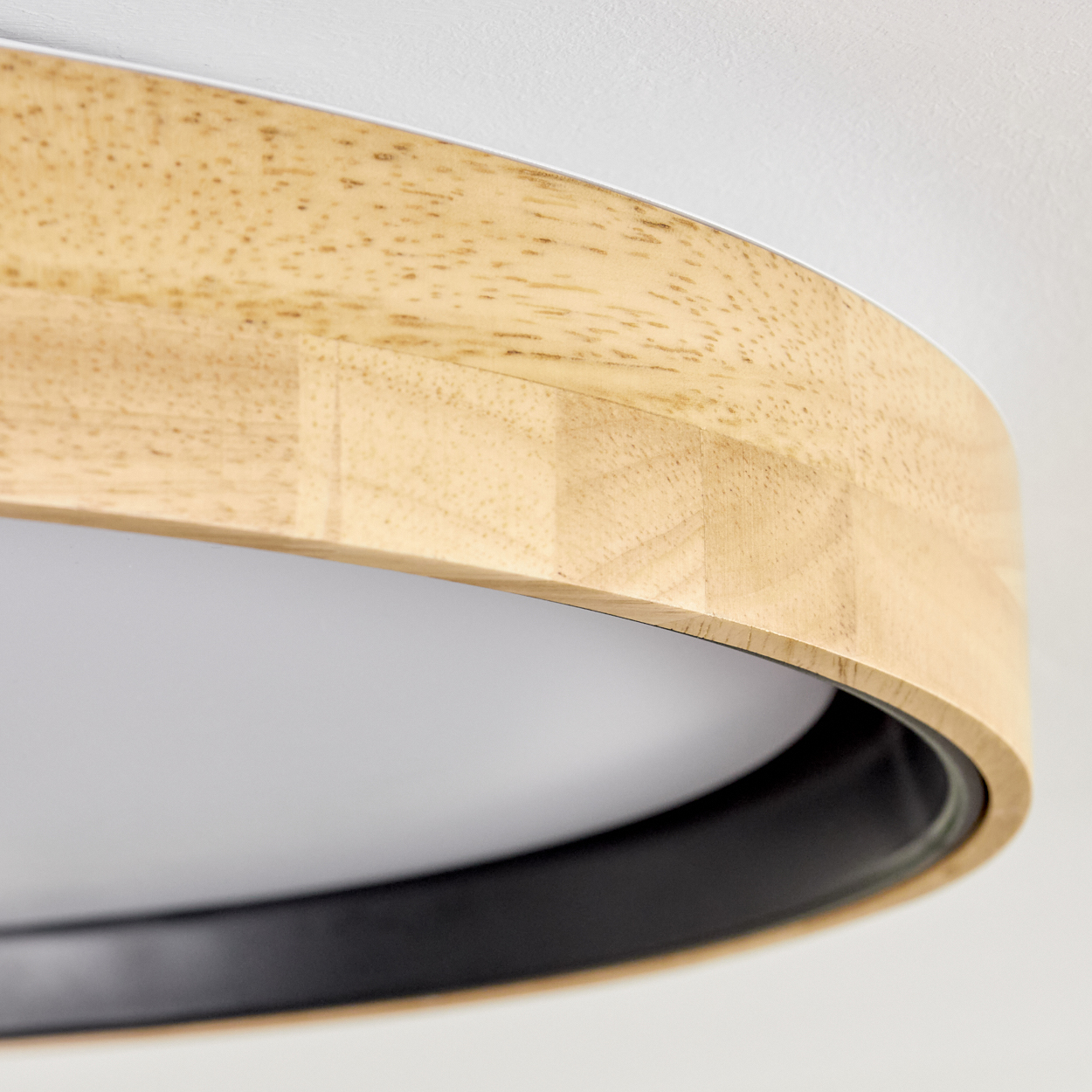 Nahaufnahme einer Deckenlampe aus Holz. Sie hat einen hellen Holzrahmen, einen schwarzen Innenring und ein weißes Innere. Der Hintergrund ist weiß.