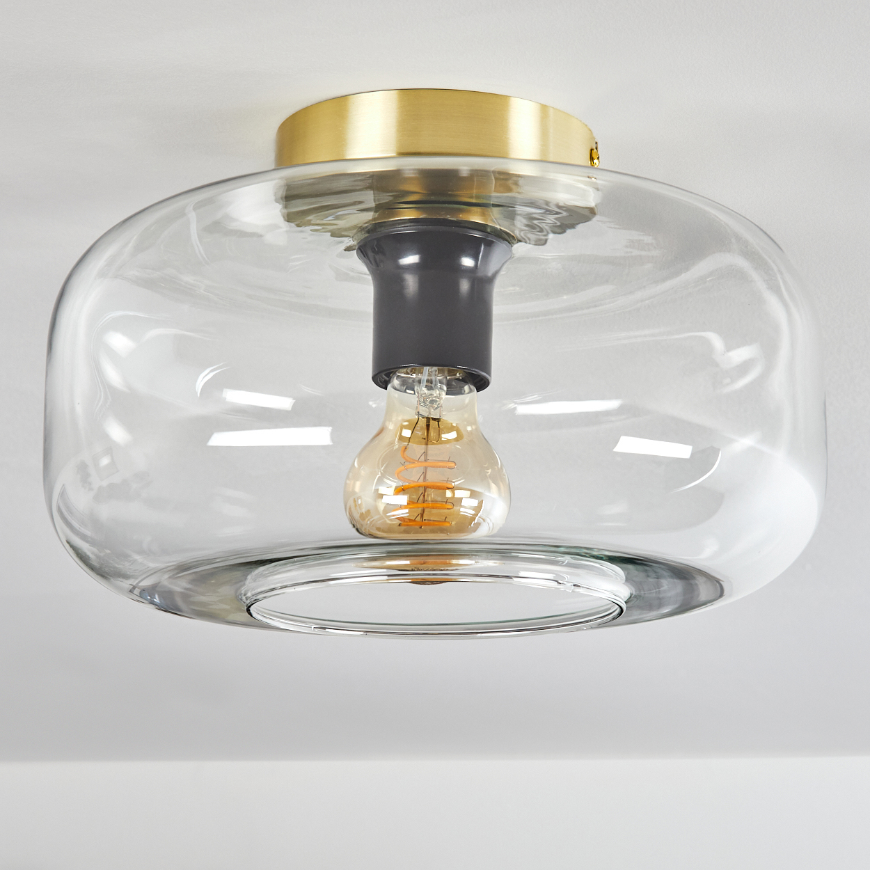 Eine moderne Deckenleuchte. Sie hat einen transparenten Glasschirm, eine goldfarbene Metallkappe und eine sichtbare Glühbirne.