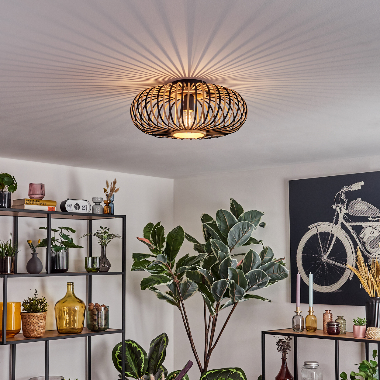 Ein modernes Wohnzimmer mit einer stilvollen Deckenlampe. Regale mit Pflanzen und Dekoration. Eine große Pflanze und ein Kunstwerk eines Fahrrades sind sichtbar.