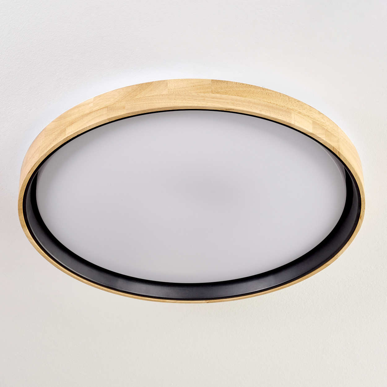 Eine runde Deckenleuchte. Sie hat einen äußeren Holzring, einen schwarzen Innenring und einen weißen Lichtdiffusor in der Mitte.