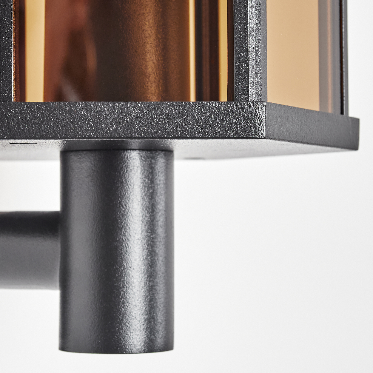 Nahaufnahme einer schwarzen Außenleuchte. Sie hat einen quadratischen Kopf mit braunen Glasscheiben. Die Lampe steht vor weißem Hintergrund.