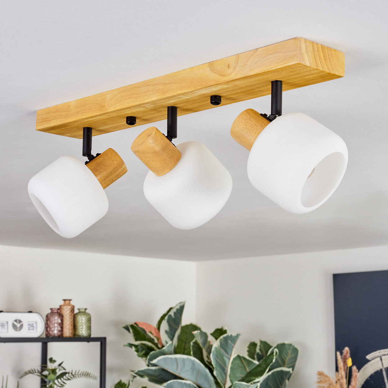 Deckenleuchte mit drei weißen Lampen, Holzakzenten und Holzbalken. Darunter Pflanzen und Dekorationsartikel.