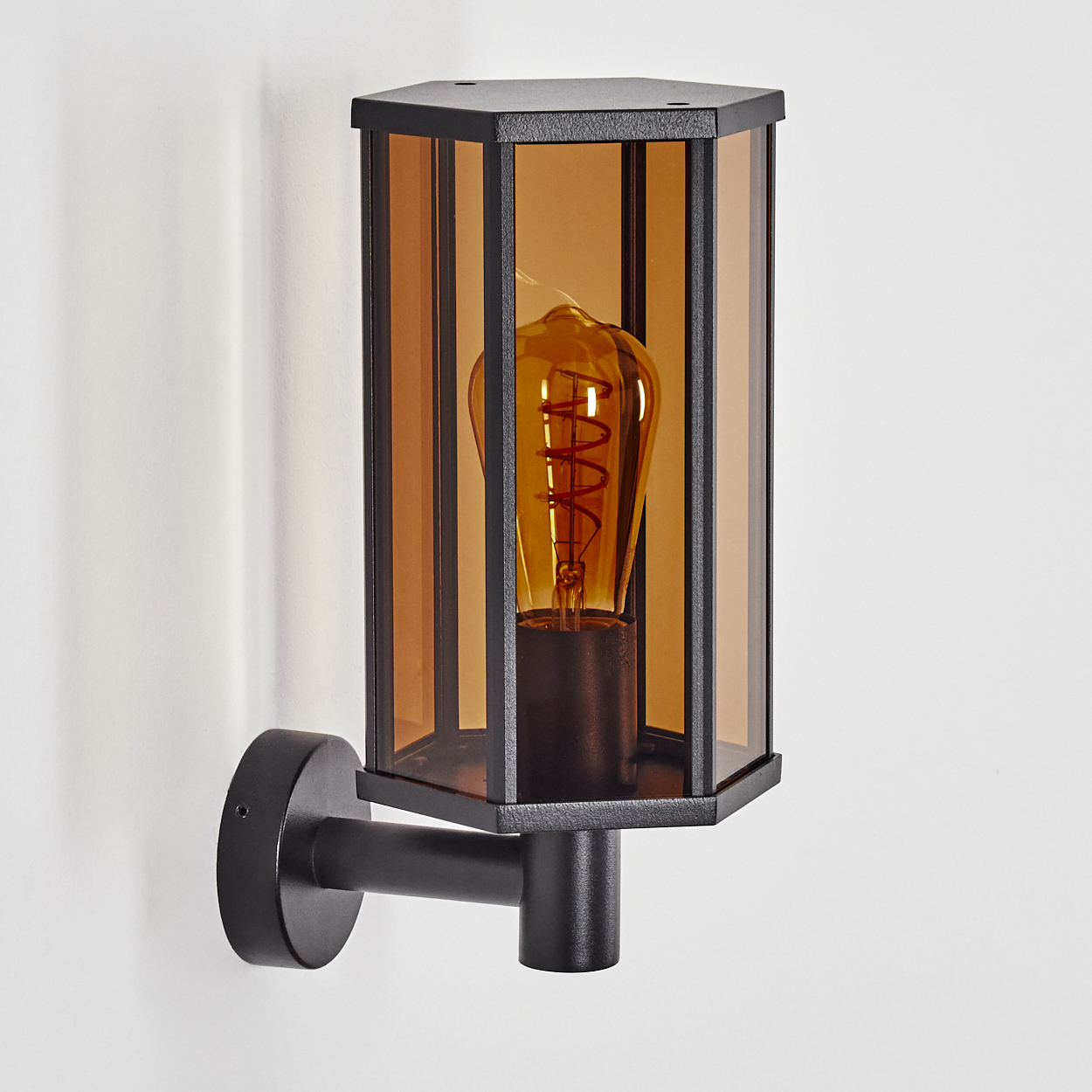 Eine schwarze Wandleuchte mit braun getöntem Glasschirm und sichtbarer Glühbirne. Sie ist an einer weißen Wand montiert.