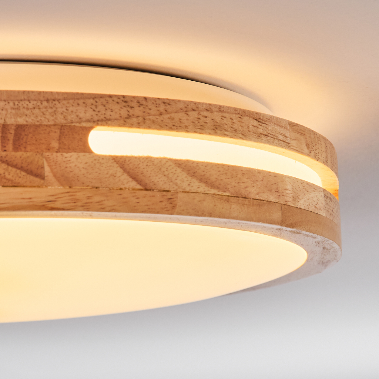 Nahaufnahme einer Deckenlampe aus Holz. Sie hat ein kreisförmiges Design mit Holzrahmen und hellem Licht in der Mitte. Der Hintergrund ist weiß.