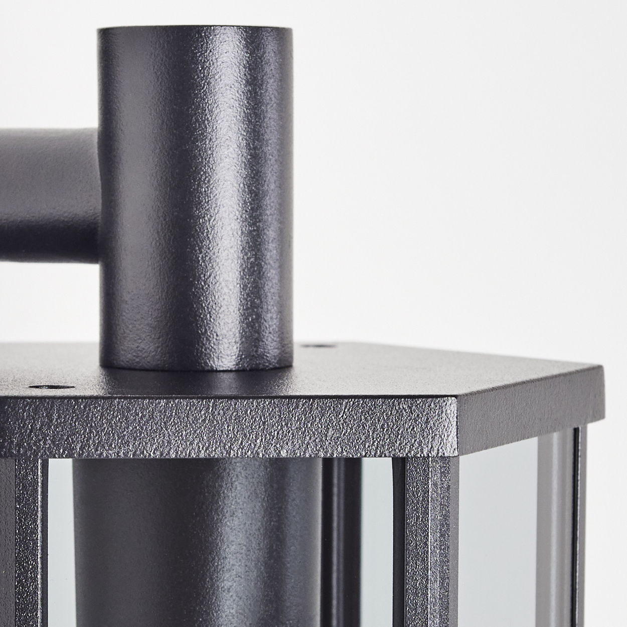 Nahaufnahme einer schwarzen Metalllampe. Die Lampe hat einen zylindrischen Oberteil und eine sechseckige Basis mit Glasscheiben. Weißer Hintergrund.