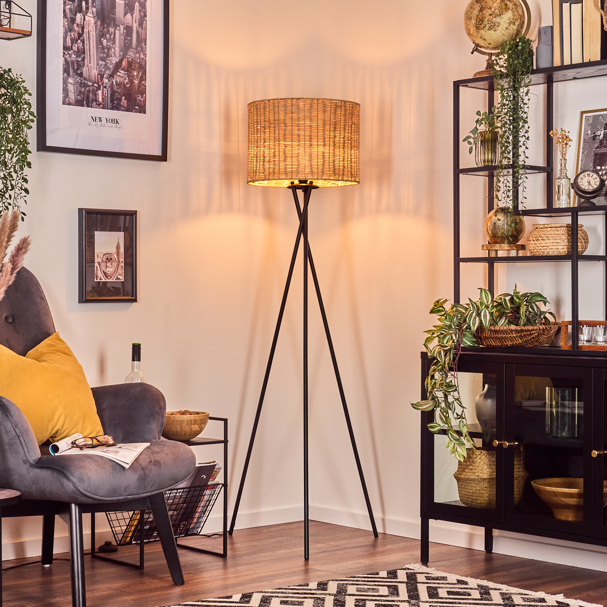Ein Wohnzimmer mit einem schwarz-weiß gemusterten Teppich, einer Korblampe, einem grauen Sessel und einem schwarzen Vitrinenschrank.