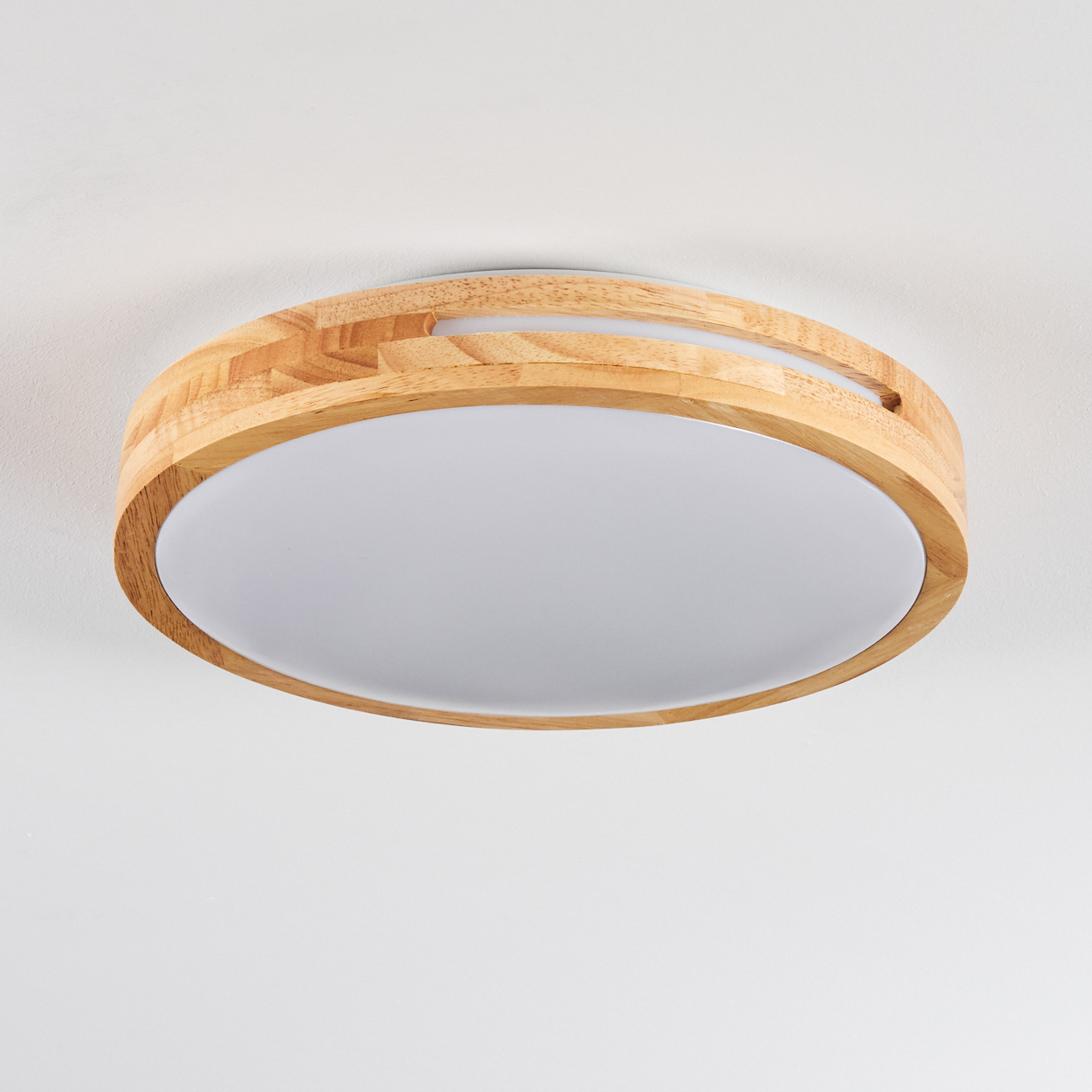 Eine runde Deckenlampe aus Holz mit weißem Diffusor. Das Holz ist hellbraun. Die Decke ist weiß.