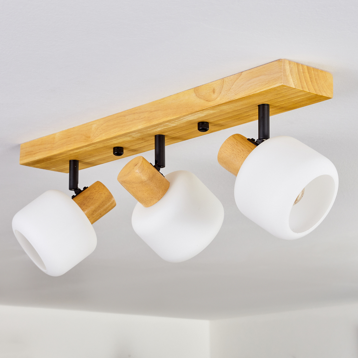 Eine Deckenleuchte mit drei weißen, quadratisch geformten Lampen, die an einem Holzbalken befestigt sind, mit Holz- und schwarzen Akzenten.