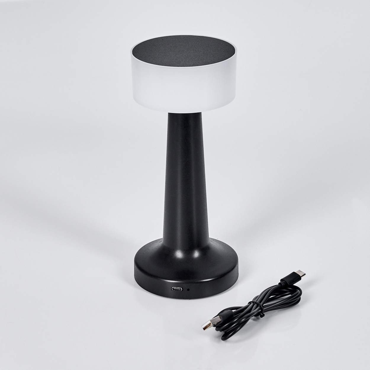 Eine schwarz-weiße Tischlampe mit USB-Kabel auf weißem Untergrund. Die Lampe hat eine kreisförmige Ober- und Unterseite.