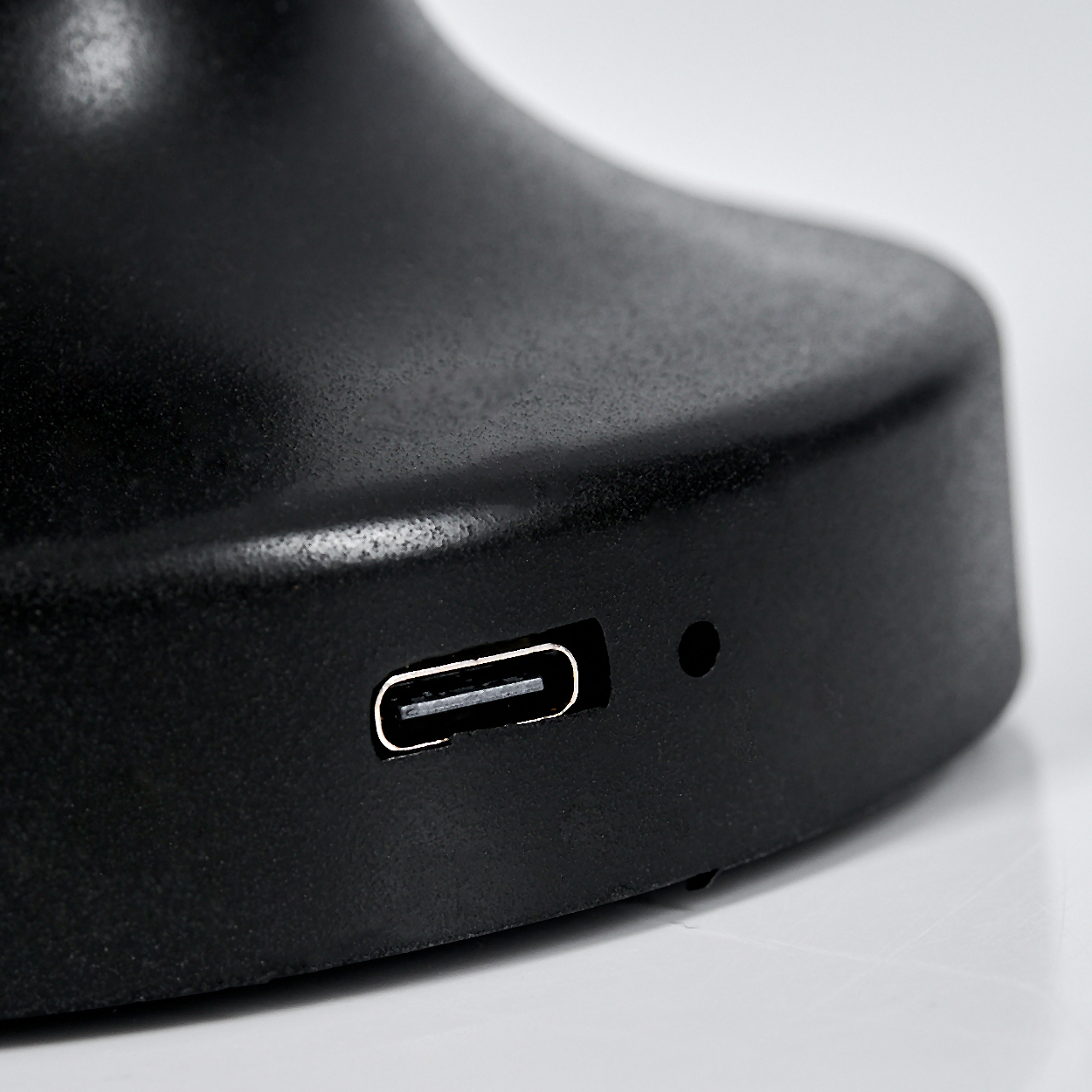 Nahaufnahme eines schwarzen Objekts mit einem USB-C-Anschluss und einem kleinen Loch auf einer weißen Oberfläche.