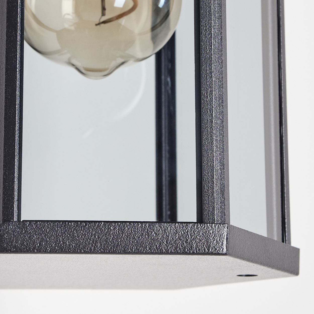 Nahaufnahme einer schwarzen Metalllaterne mit Glasscheiben und einer Glühbirne im Inneren. Der Hintergrund ist weiß.