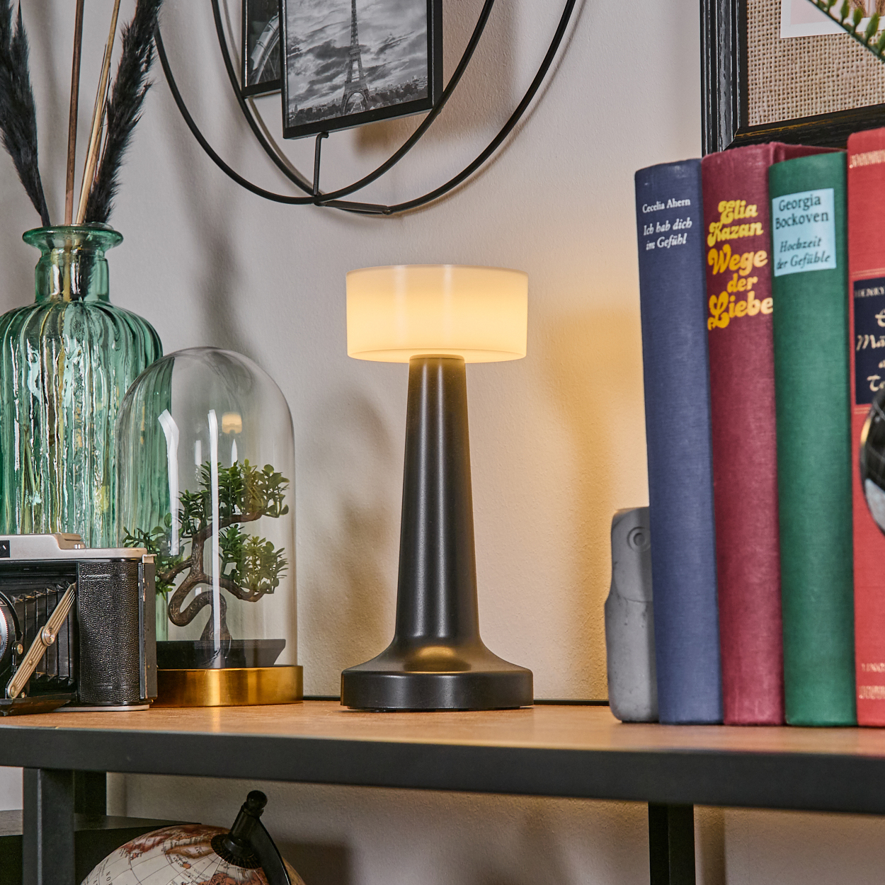 Eine Tischlampe, Bücher, eine Kamera, ein Globus und dekorative Gegenstände stehen auf einem Holzregal und schaffen eine gemütliche Atmosphäre.