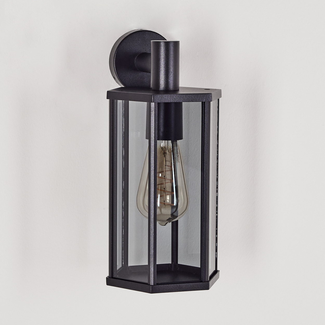 Eine schwarze Wandlampe mit Glasgehäuse und sichtbarer Glühbirne ist an einer weißen Wand montiert.